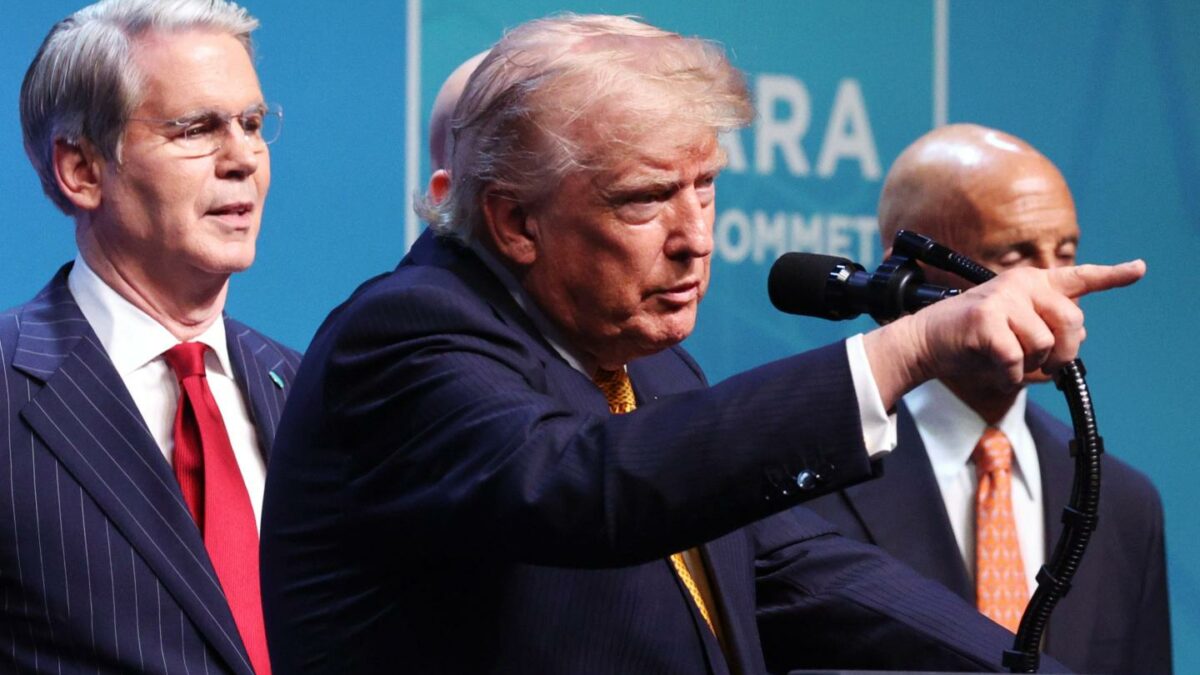 Donald Trump, standing behind a podium, points in front of him with Scott Bessent standing behind him.
