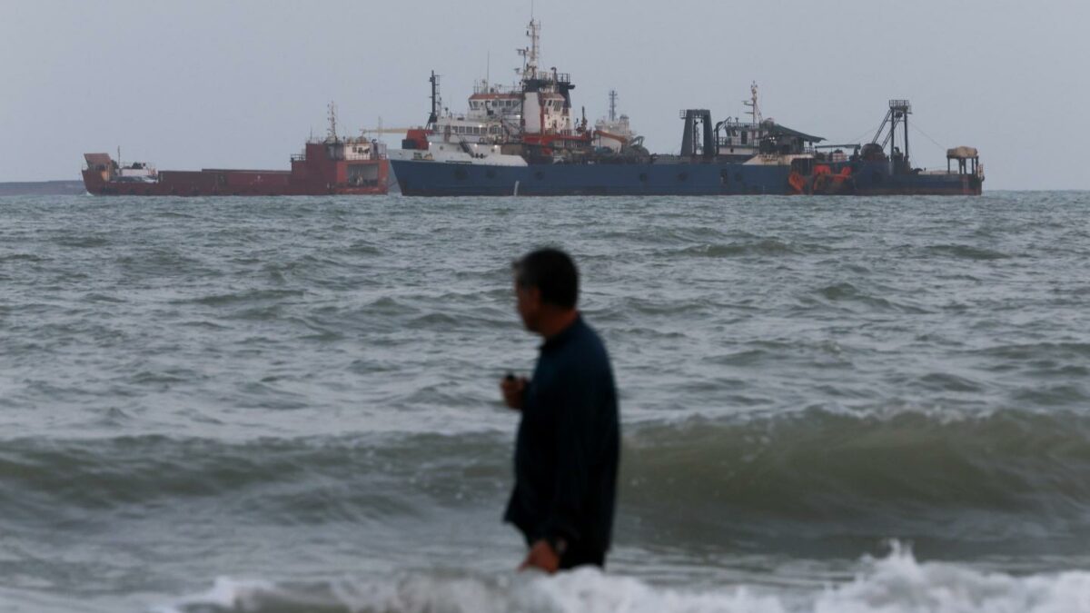 BANDAR ABBAS, IRAN - A person wades in the water as ships are seen anchored in the Strait of Hormuz on Aug. 10, 2026 off the coast of Bandar Abbas, Iran. In a recent statement, Iran's Supreme National Security Council said the vital waterway would not reopen until the United States corrects its behavior, demanding that the U.S. end its war on Iran and compensate the country for war damage, among other conditions. Iran has largely halted vessel traffic through the strait with the threat of strikes; meanwhile, the U.S. has imposed a blockade on Iranian ports.
