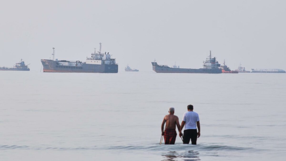 Two men wade in the waters of the Strait of Hormuz with vessels anchored in the background, off Bandar Abbas, Iran, Sunday, July 12, 2026.