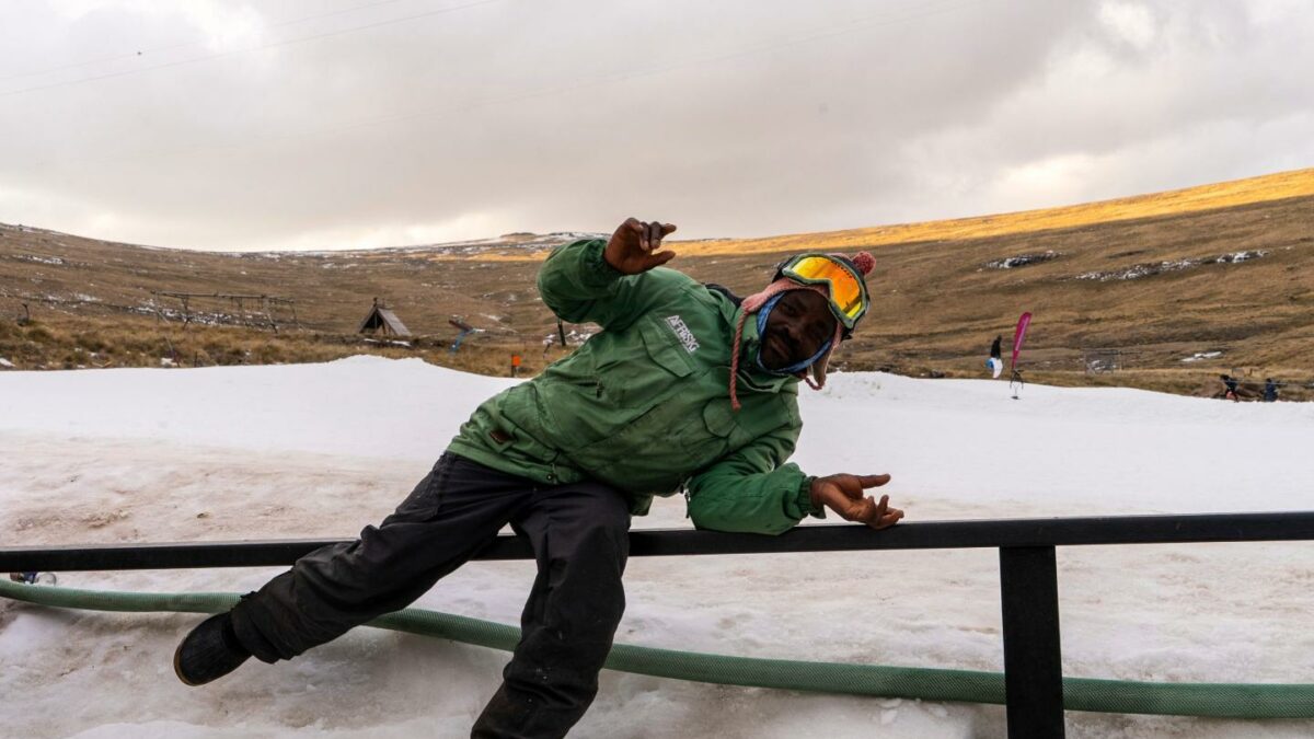 A ski worker in winter skiing gear strikes a pose in front of a ski slope in Lesotho.
