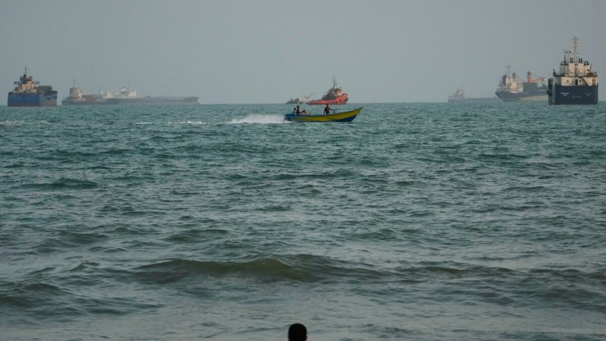 A swimmer remains near the shore as a motorboat passes commercial vessels anchored in the Strait of Hormuz off Bandar Abbas, Iran, Friday, Sept. 4, 2026.