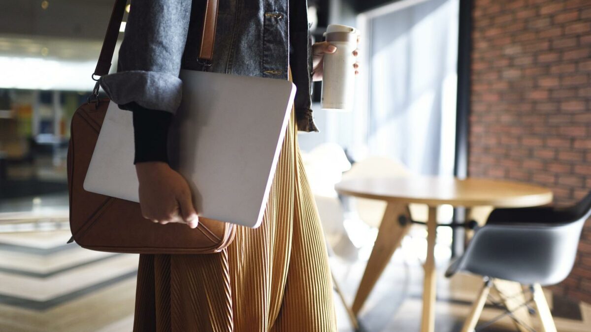 A person holding a laptop in a coffee shop.