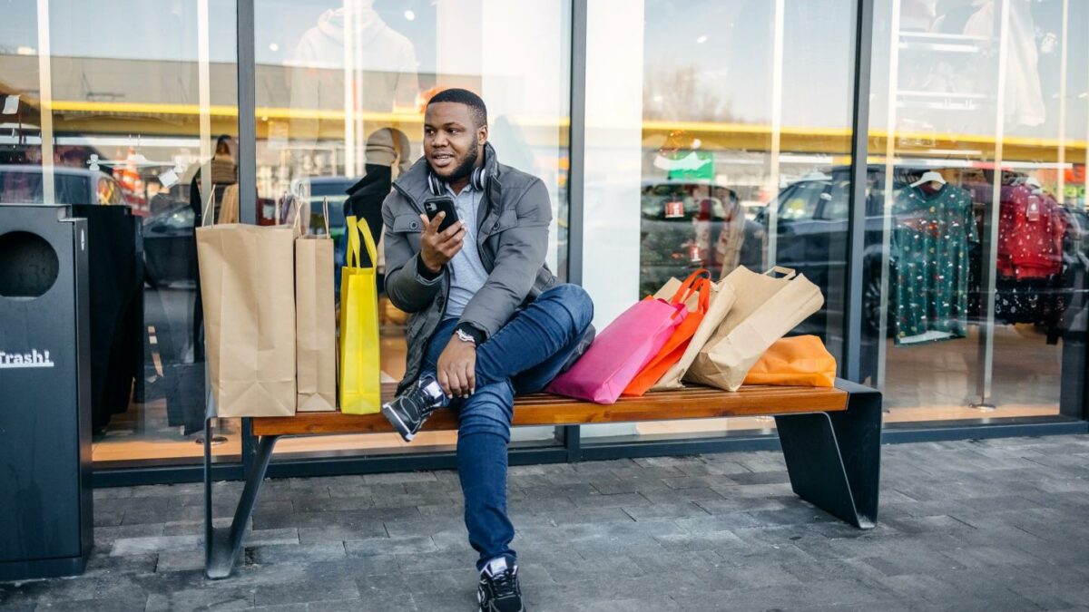 A man waits outside a store with shopping bags.