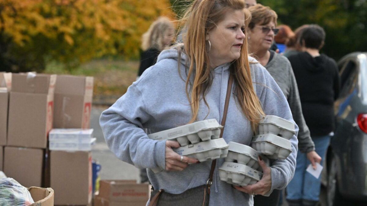 A woman in a grey hoodie holds six cartons of eggs in her arms.