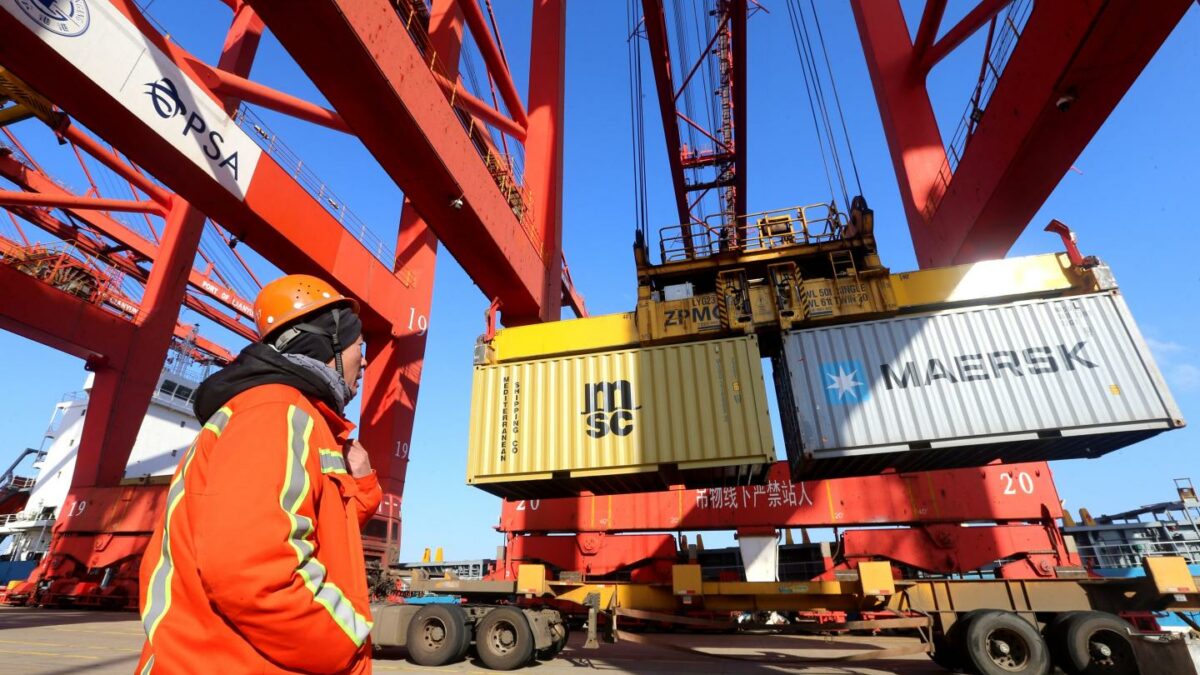 A dock workers watching a crane hoist up shipping containers.