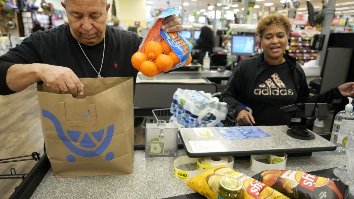 A man bags groceries in the check-out line, and a woman stands next to him.