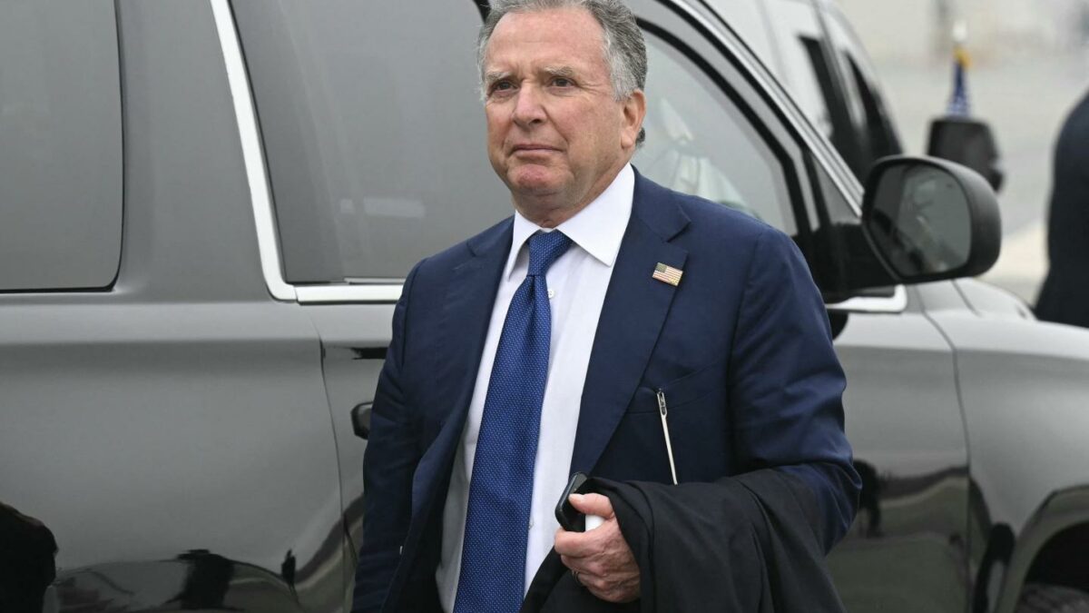 Steve Witkoff walks in front of a car dressed in suit and tie with his phone in his hand and his jacket draped over his arm.