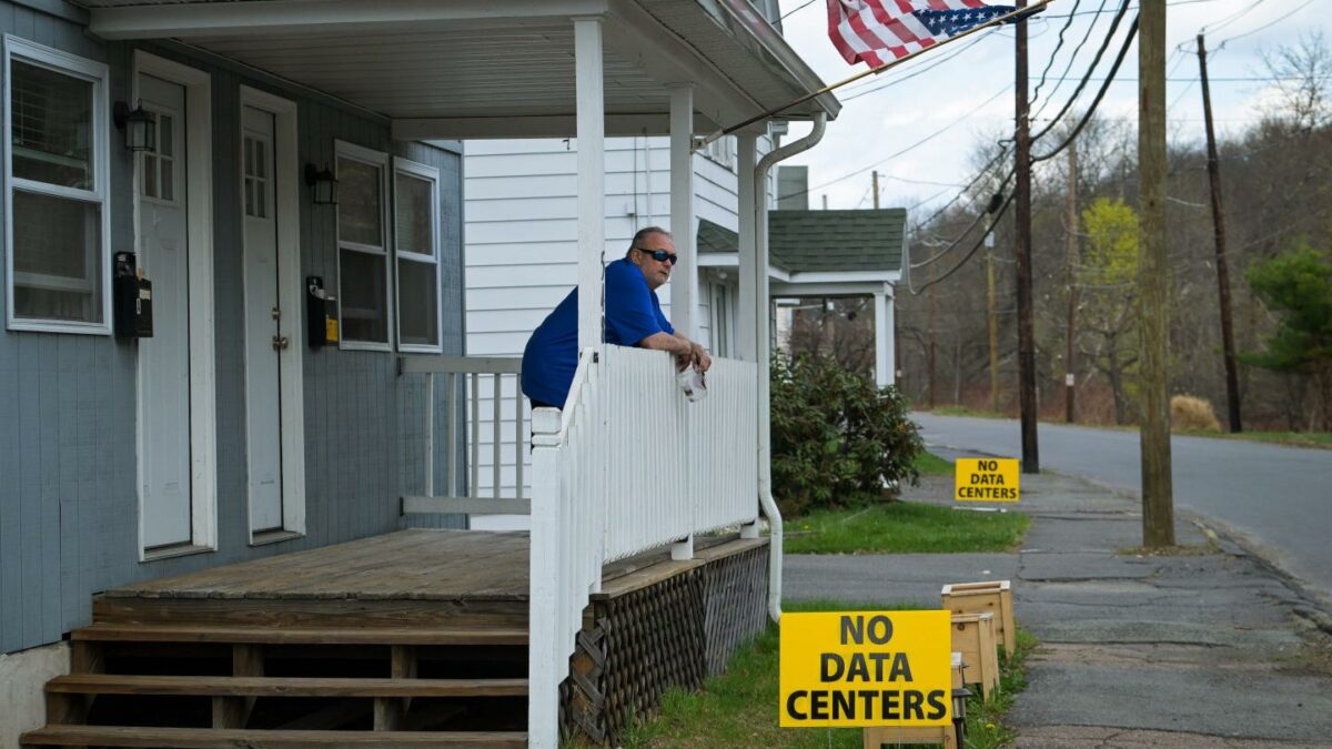 A man stands looking out over his front porch where a sign reads, "No data centers."