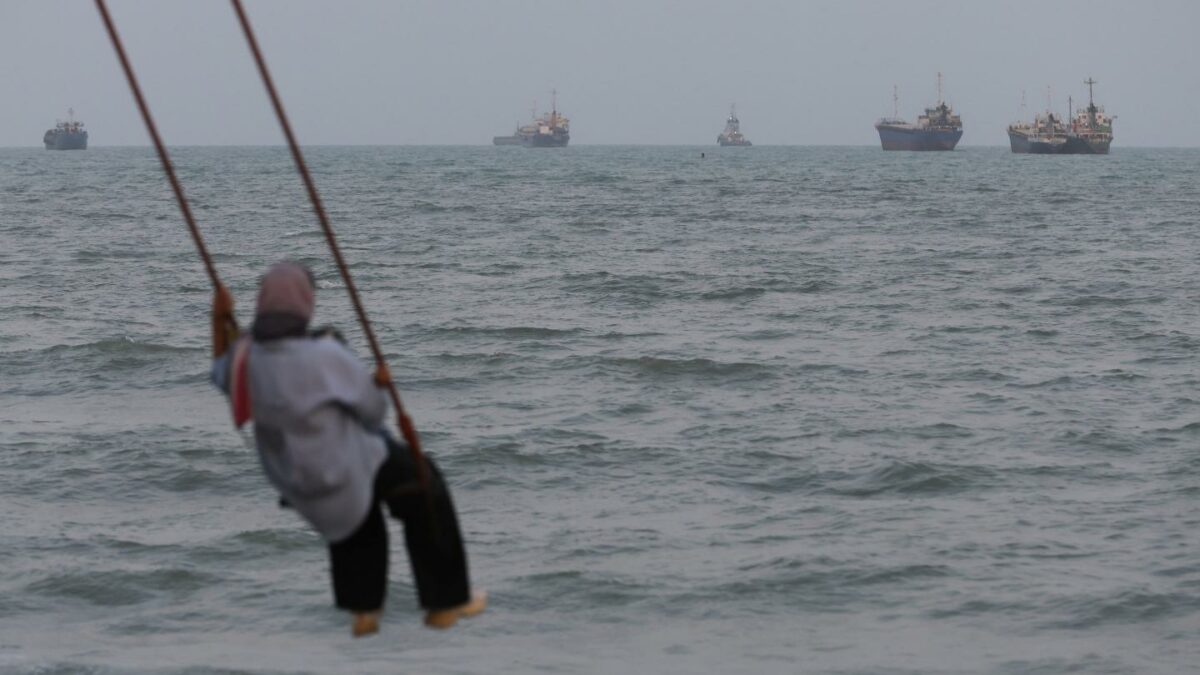 BANDAR ABBAS, IRAN - A person swings over the shoreline as ships are seen anchored in the Strait of Hormuz on Aug. 10 off the coast of Bandar Abbas, Iran. In a recent statement, Iran's Supreme National Security Council said the vital waterway would not reopen until the United States corrects its behavior, demanding that the U.S. end its war on Iran and compensate the country for war damage, among other conditions. Iran has largely halted vessel traffic through the strait with the threat of strikes; meanwhile, the U.S. has imposed a blockade on Iranian ports.