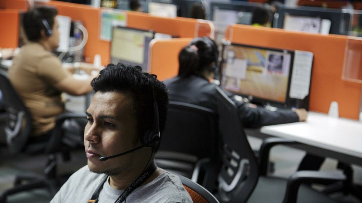 A man with a headset sits at a desk in a call center.