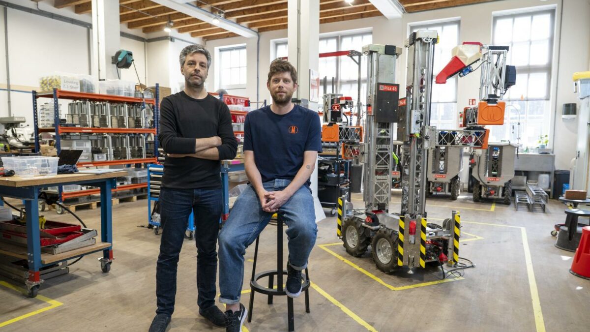 Salar al Khafaji stands while Sebastiaan Visser sits on a stool in front of a robotics warehouse